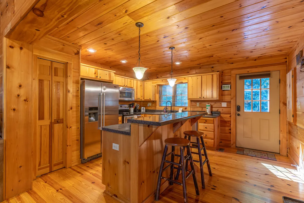 A warm, welcoming kitchen scene featuring an island with bar stools, stainless steel appliances, and a front door with a window, hinting at direct access to outdoor spaces.