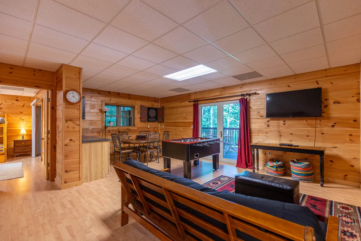 This image captures the heart of the lodge’s main level open-concept space. The foreground features a comfortable sofa set up for relaxation, with a foosball table highlighting opportunities for fun game nights. The dining area is visible in the background, set next to large sliding doors that let in natural light and offer easy access to the outdoors, perfectly representing the flow between indoor gathering and outdoor adventure.