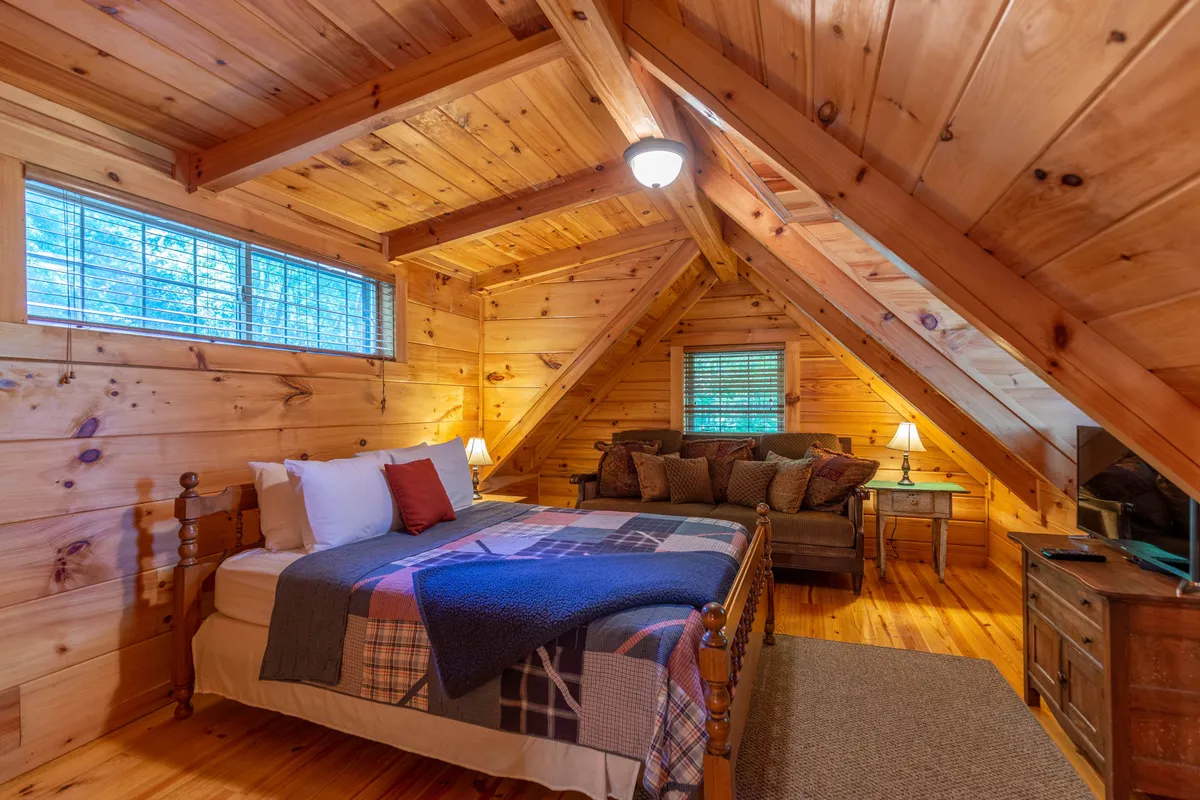 The photo showcases a comfortable living area with a bed, sofa, wooden beams, and multiple windows. The presence of windows hints at abundant natural light and the potential for guests to observe seasonal scenery from inside. The room appears ideal for relaxing with a book or sharing stories after a day exploring the mountains.