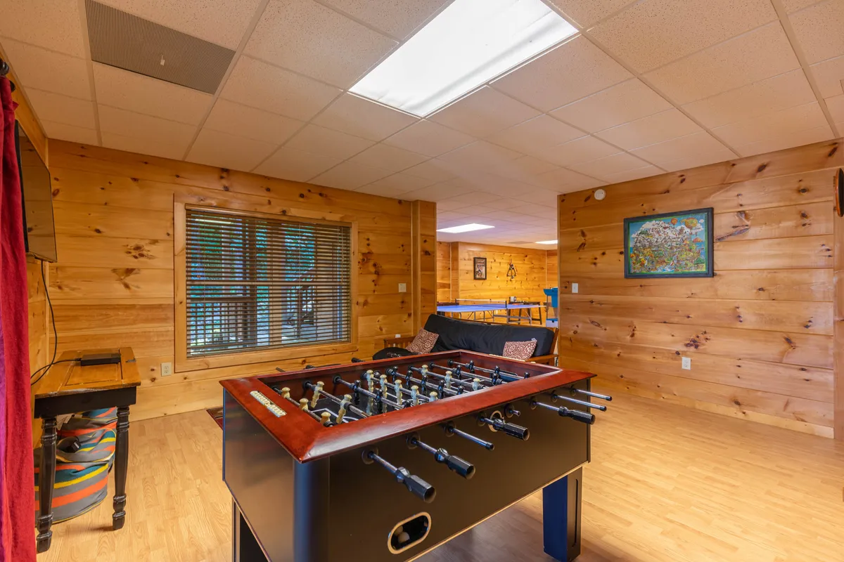 A cozy corner featuring a foosball table, a comfortable sofa, wall art, and a window with blinds. The relaxed setup encourages both active play and laid-back socializing.