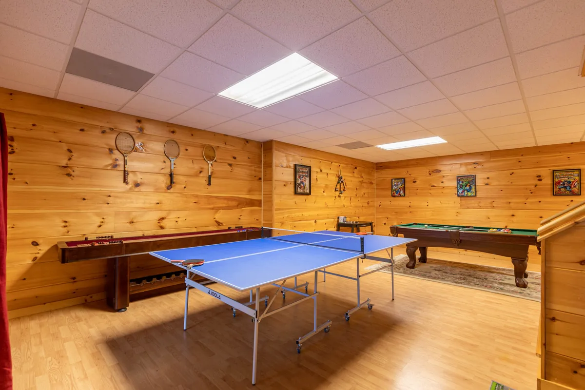 The photo showcases a vibrant recreation space with a ping pong table, pool table, and colorful artwork on the walls. The wooden paneling and decorative rackets evoke a playful, energetic atmosphere, ideal for memorable game nights with friends or family.