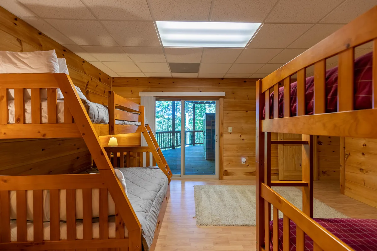 A playful bunk room with wooden walls and a large sliding door, opening to the outside or a deck. The space feels inviting and relaxed, ideal for family gatherings and for pets to lounge nearby.
