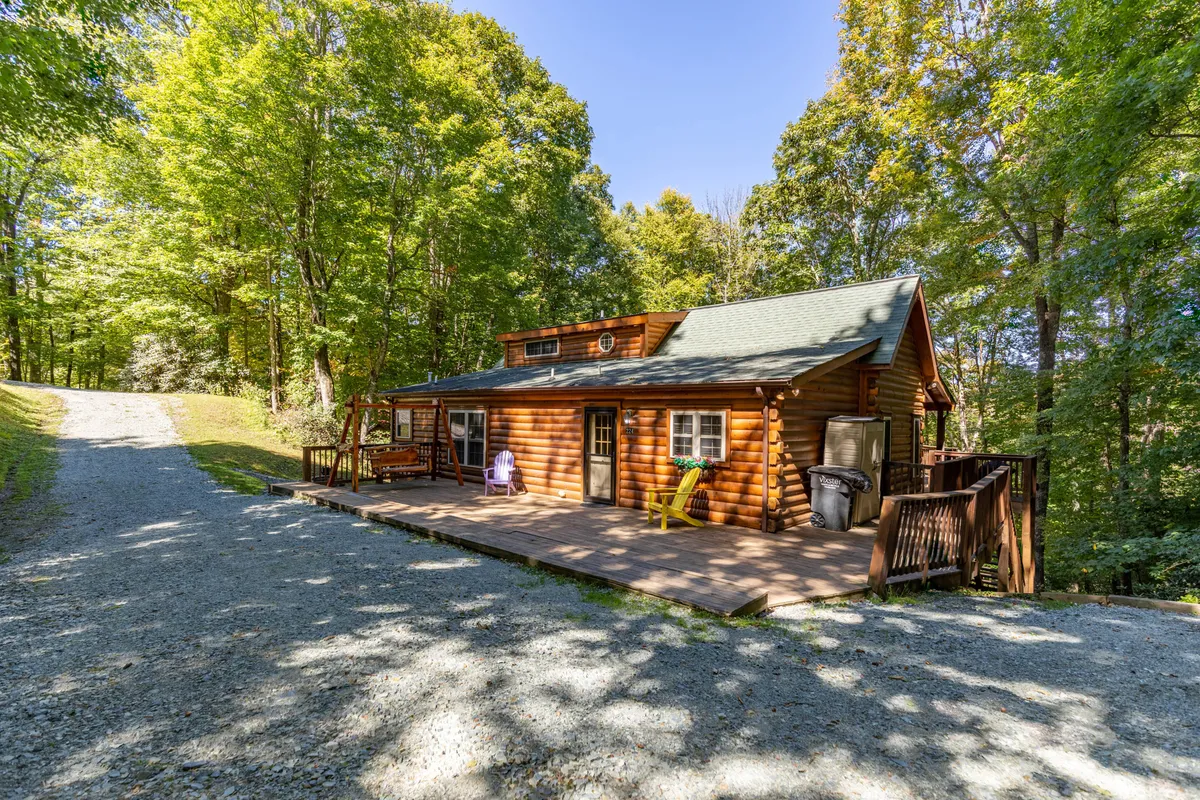 This image captures the log cabin amid a forested setting, focusing on the expansive deck and the surrounding trees. The scene conveys serenity and a strong sense of place, suggesting activities like watching sunsets, sipping coffee, or taking in the sights and sounds of mountain wildlife from the deck.