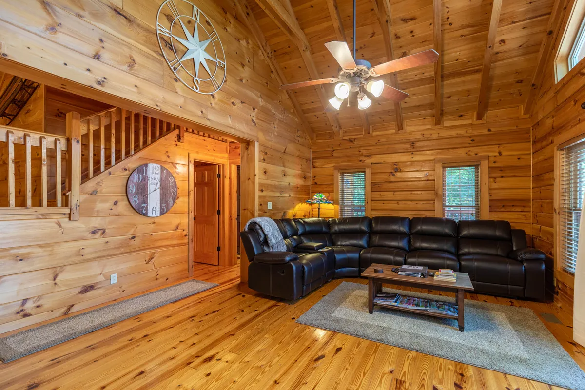 A cozy living area with a black sectional sofa, wooden coffee table, and rustic wood-paneled walls and ceiling. The room feels inviting and is adorned with cheerful decorations, perfect for relaxing after an active day spent outdoors or indoors.