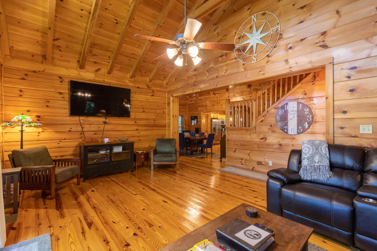 A welcoming interior scene with a wooden ceiling, leather sofa, flat-screen TV, and a large dining area in the background. The decorative clock and warm lighting enhance the cozy, rustic-chic atmosphere, ideal for both family movie nights and intimate dinners.