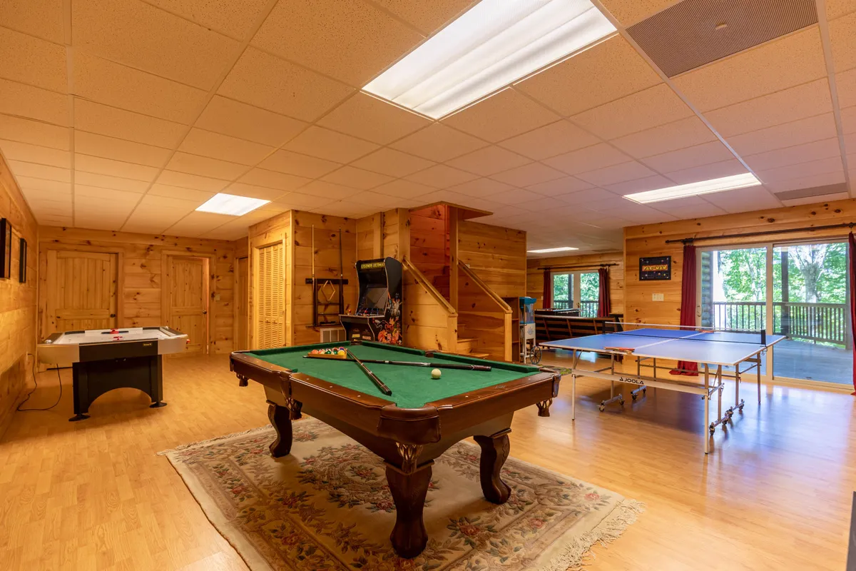 A spacious game room featuring a pool table and ping pong table set against warm wooden walls and large windows that let in natural light. The setup invites guests to participate in friendly tournaments and social gatherings, embodying the heart of family entertainment described in the section.