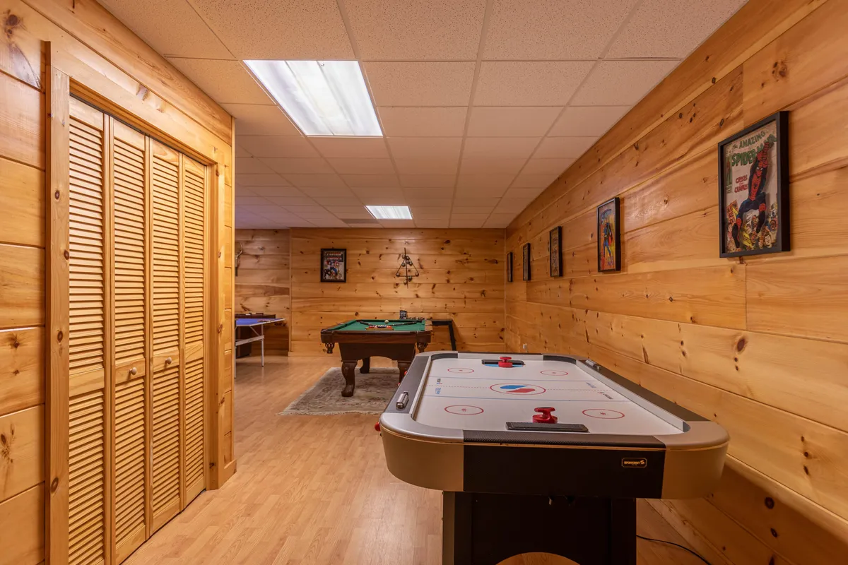 A lively interior scene with both an air hockey and pool table surrounded by wooden walls and decorated with framed posters, creating an energetic atmosphere for group play and competition.